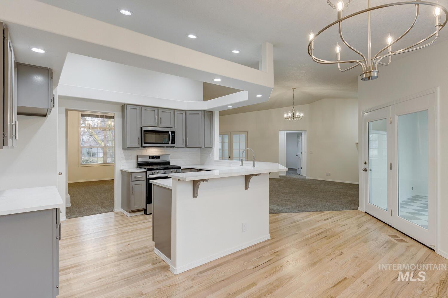 Kitchen with gray cabinets, a kitchen breakfast bar, hanging light fixtures, appliances with stainless steel finishes, and a peninsula