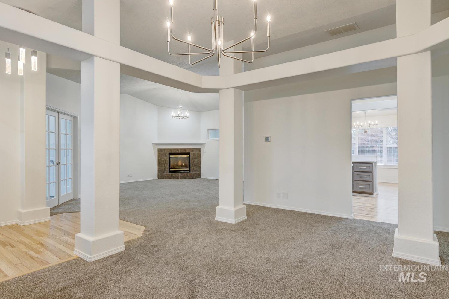 Unfurnished living room with light carpet, a tile fireplace, a chandelier, french doors, and plenty of natural light