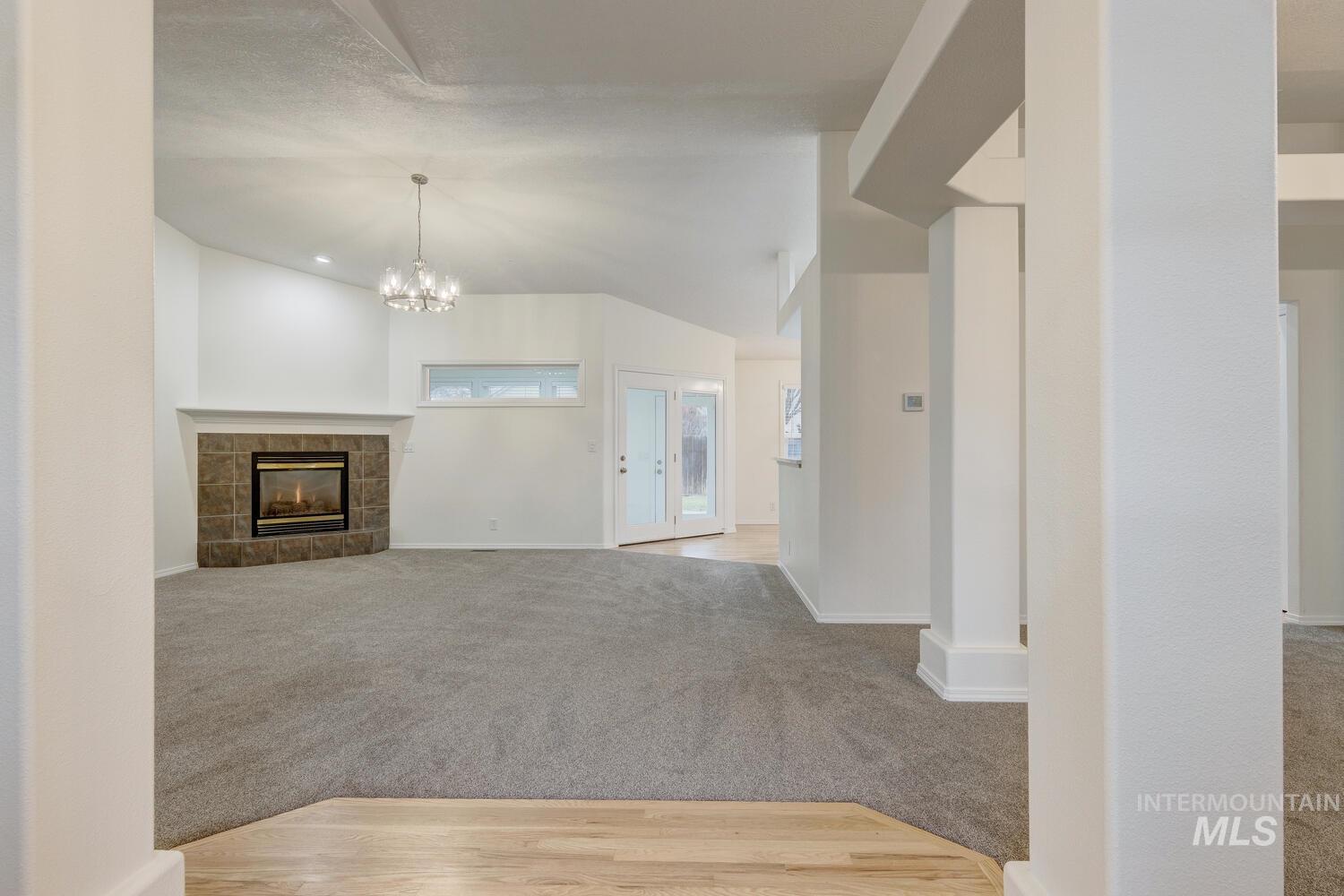 Unfurnished living room featuring a tile fireplace, light carpet, lofted ceiling, and a chandelier