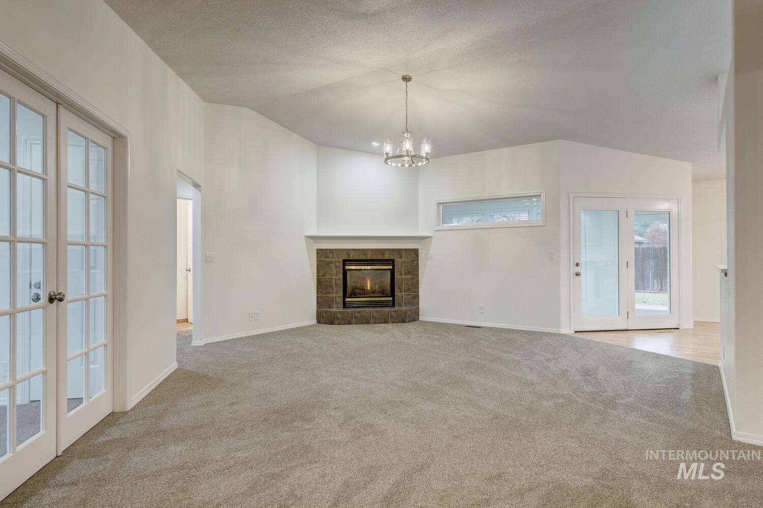 Unfurnished living room featuring vaulted ceiling, a tile fireplace, french doors, light colored carpet, and a chandelier