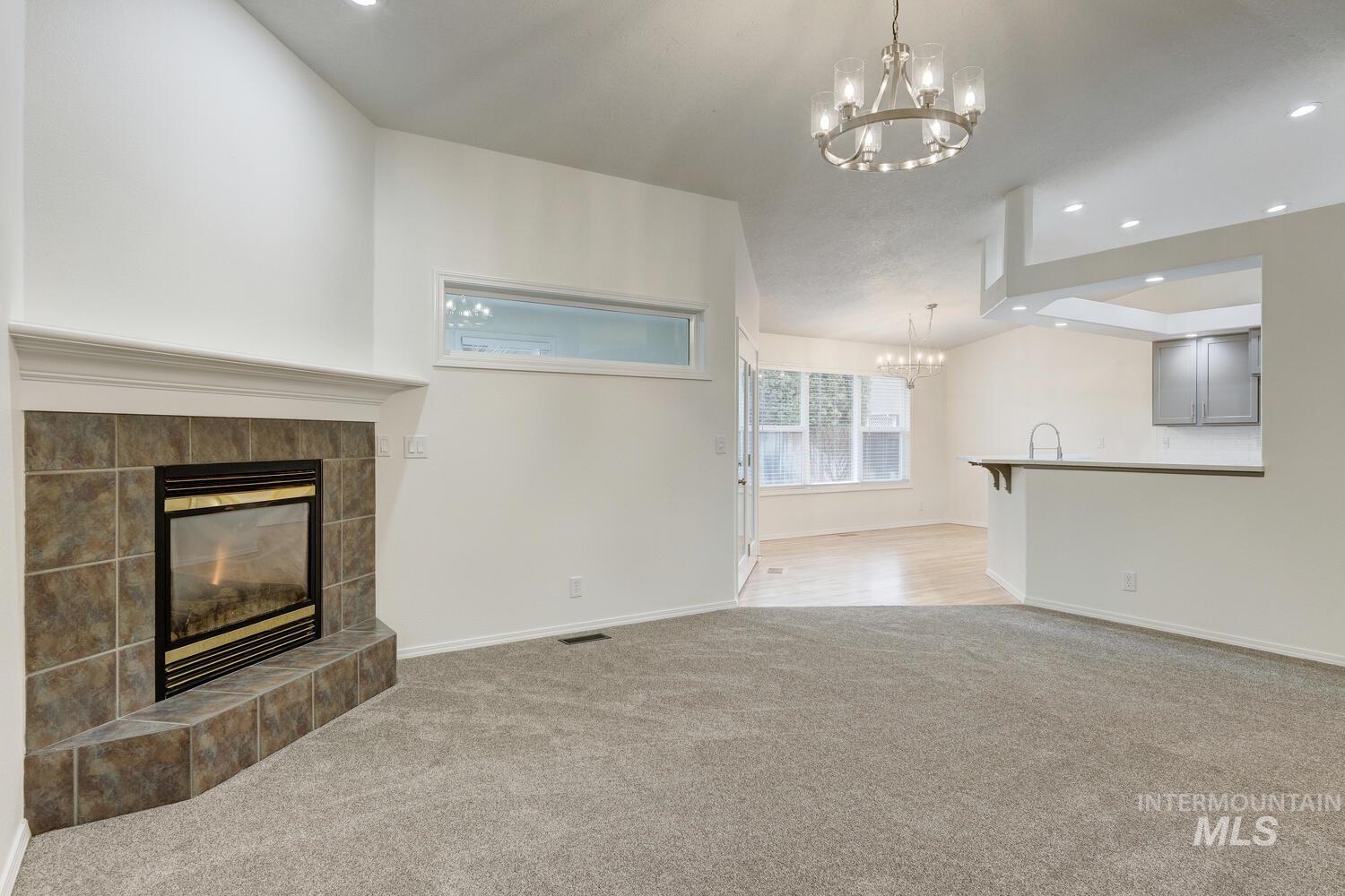 Unfurnished living room with recessed lighting, a tiled fireplace, light colored carpet, and a chandelier