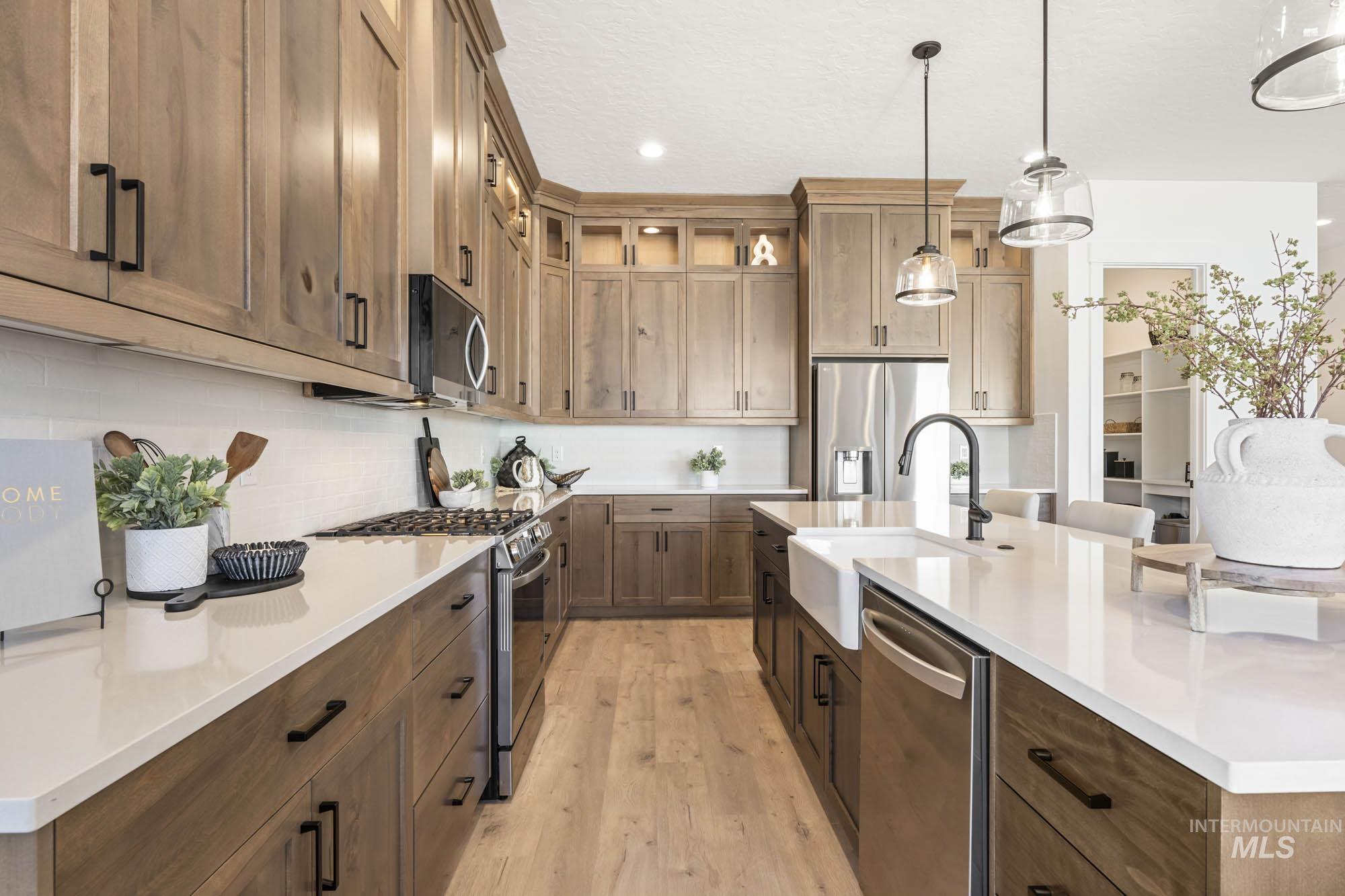 Kitchen featuring appliances with stainless steel finishes, an island with sink, hanging light fixtures, light wood-style flooring, and brown cabinets