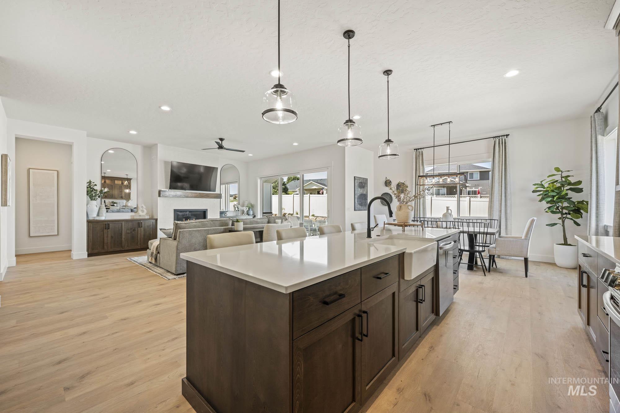 Kitchen with dark brown cabinetry, light wood-style floors, hanging light fixtures, open floor plan, and recessed lighting