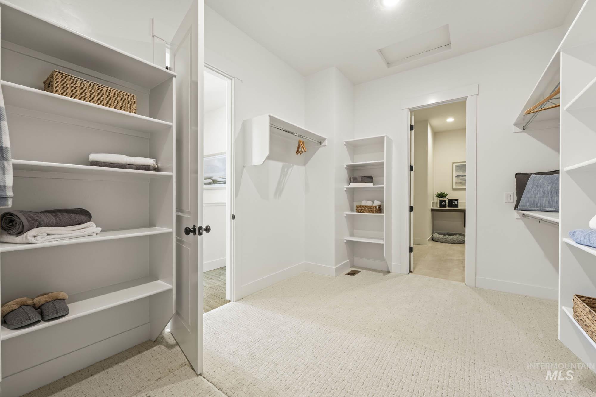 Walk in closet with attic access and light colored carpet