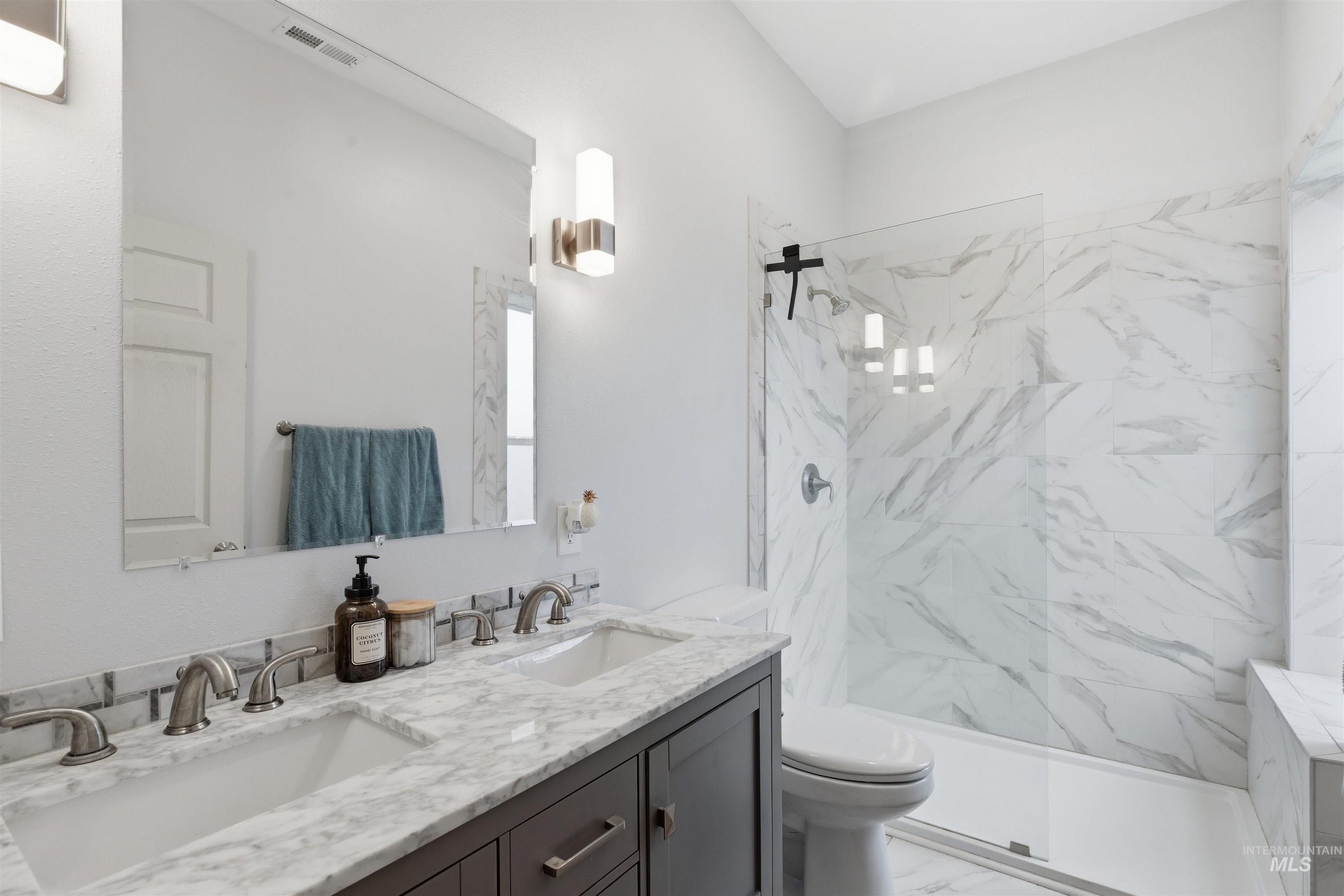 Full bathroom featuring double vanity, a marble finish shower, and light marble finish flooring