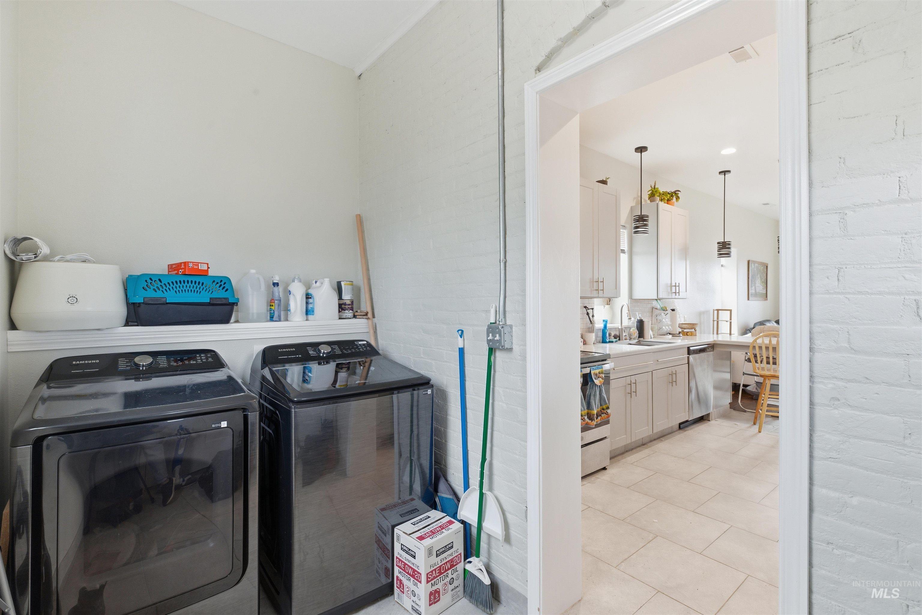 Washroom featuring brick wall, light tile patterned flooring, and washer and clothes dryer