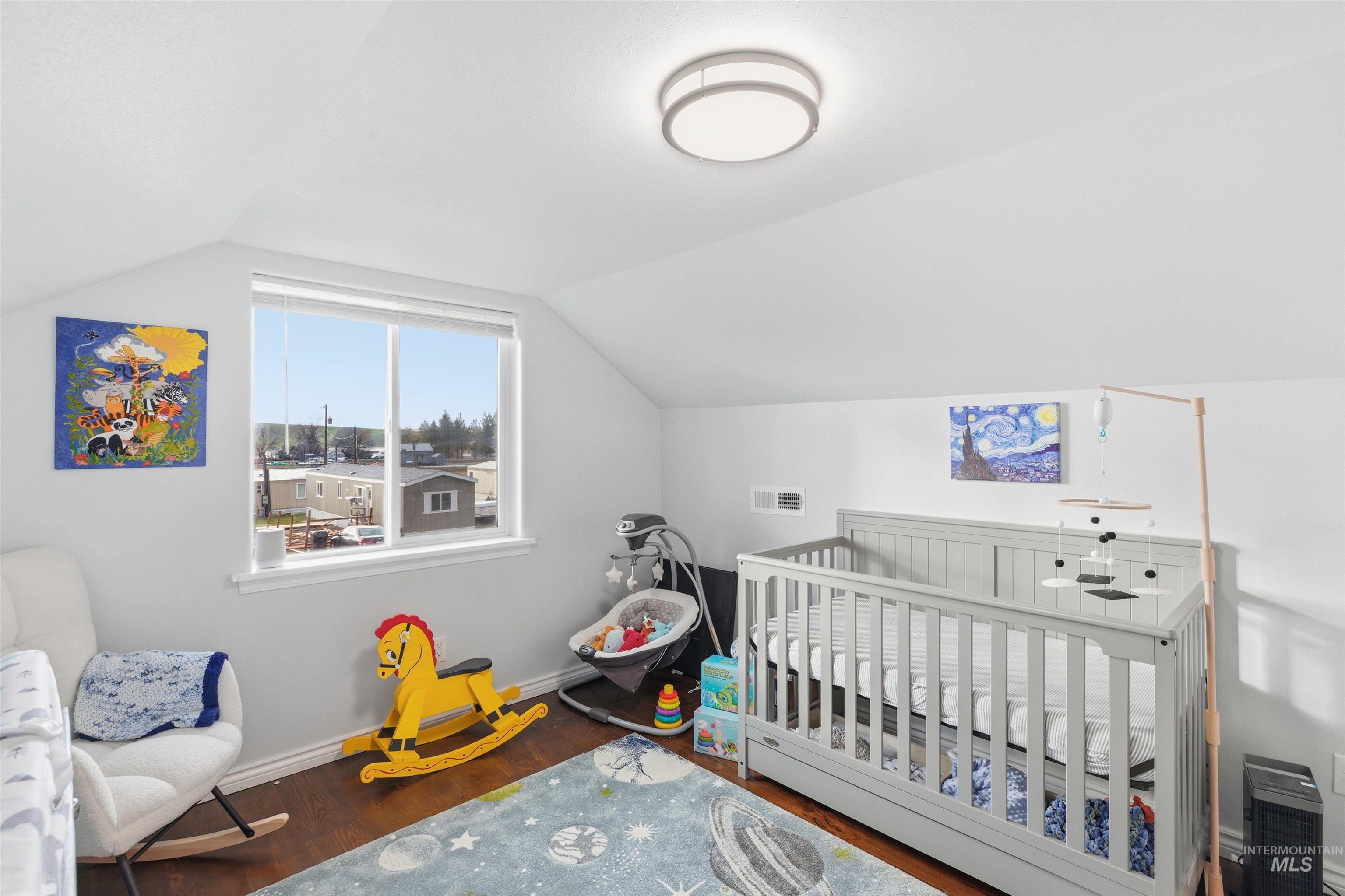 Bedroom with lofted ceiling, dark wood-type flooring, and a nursery area