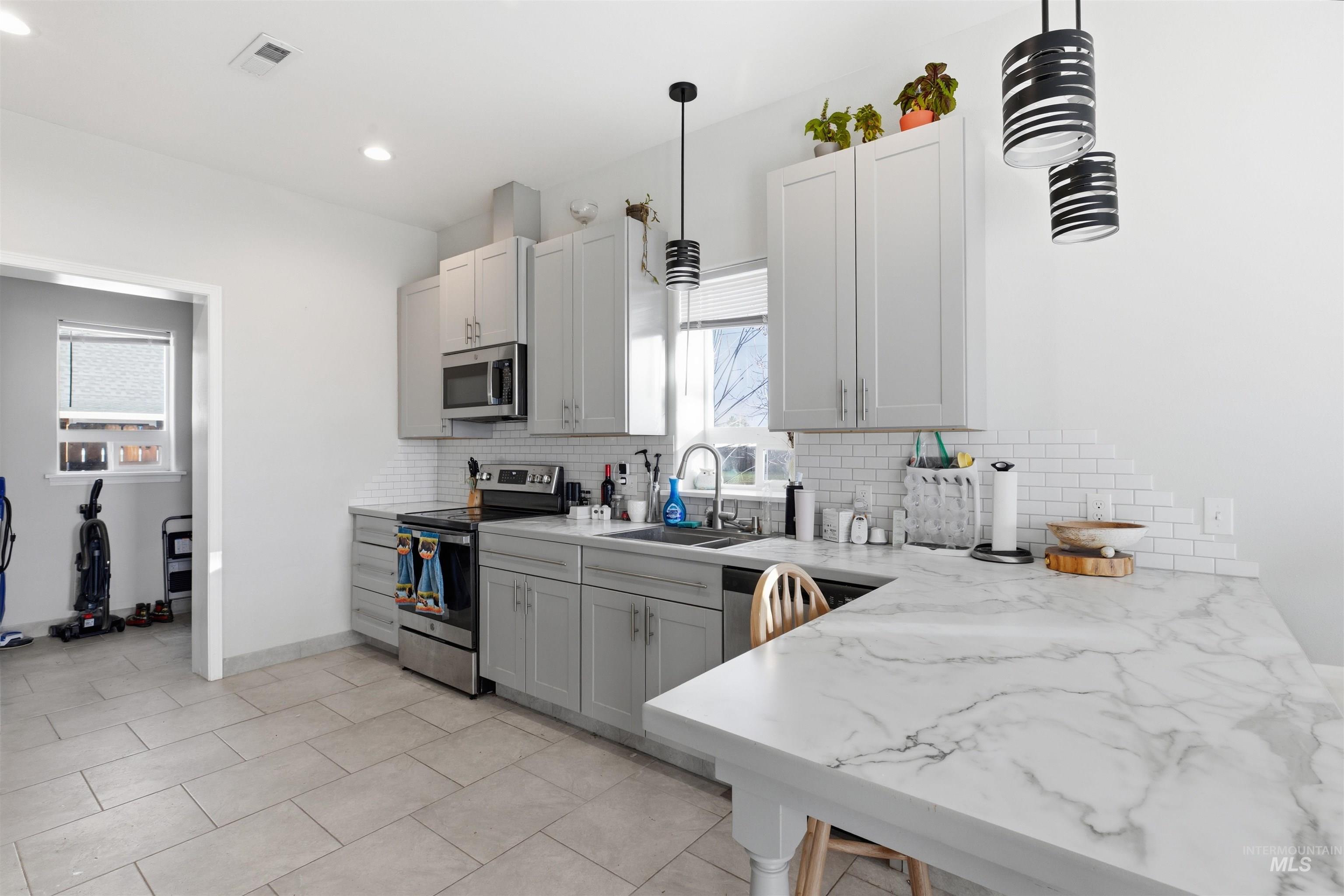 Kitchen with stainless steel appliances, light stone countertops, decorative backsplash, light tile patterned flooring, and decorative light fixtures