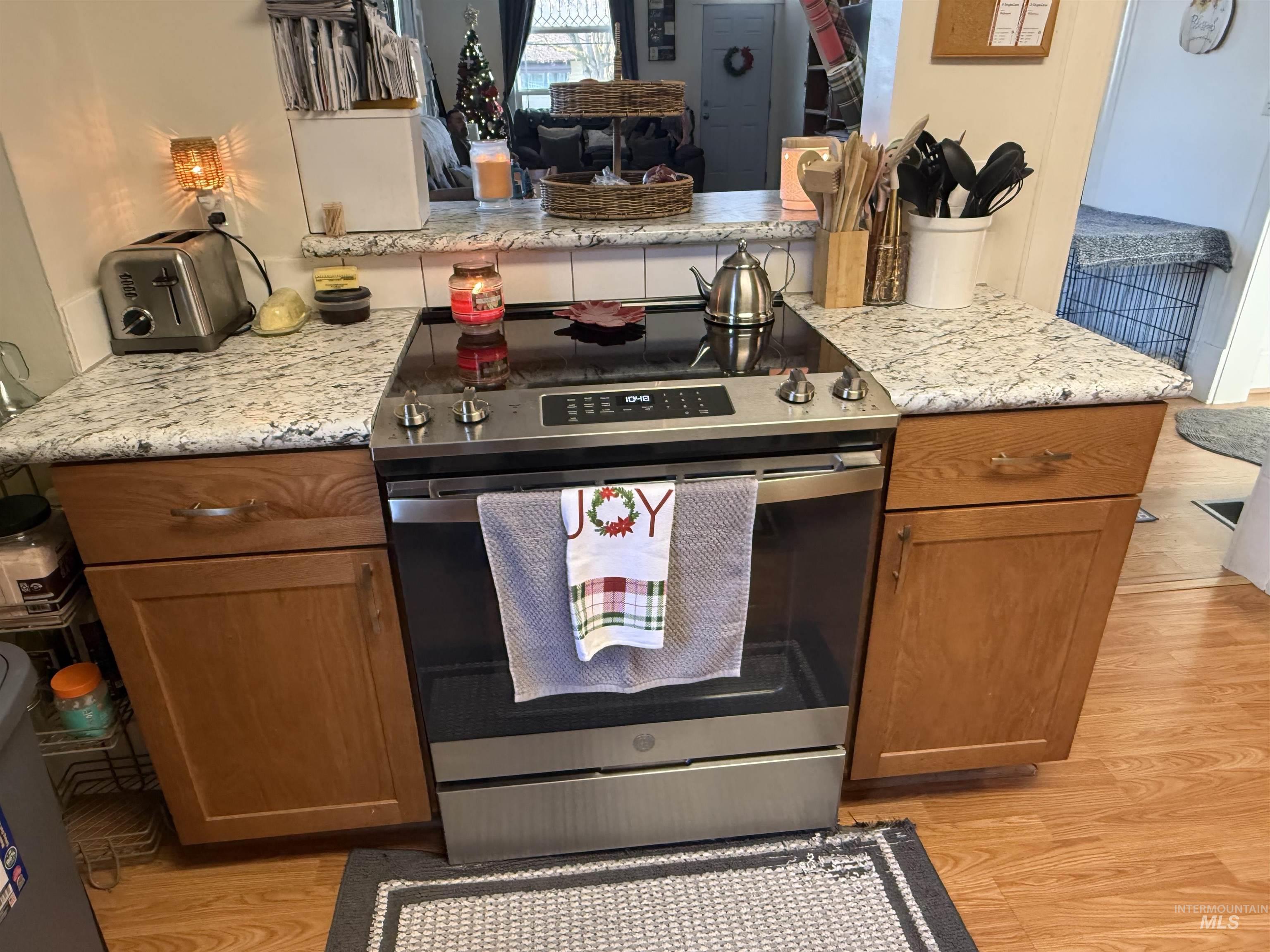 Kitchen featuring brown cabinets, stainless steel range with electric cooktop, light wood-style floors, and light stone countertops
