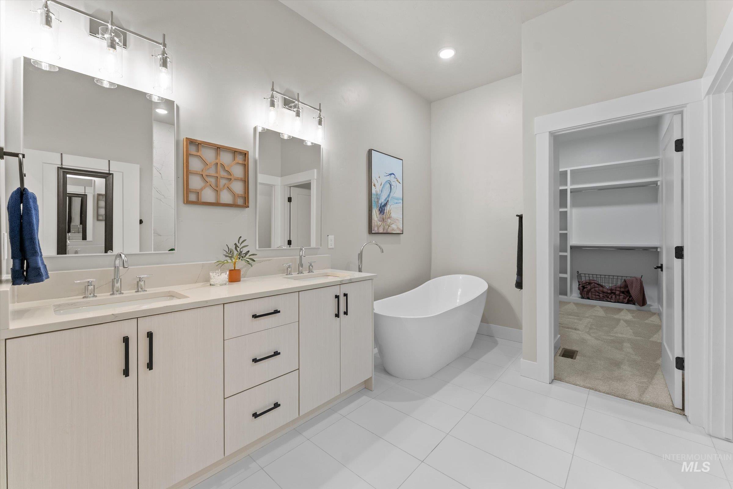 Bathroom featuring double vanity, a freestanding tub, a walk in closet, light tile patterned floors, and recessed lighting