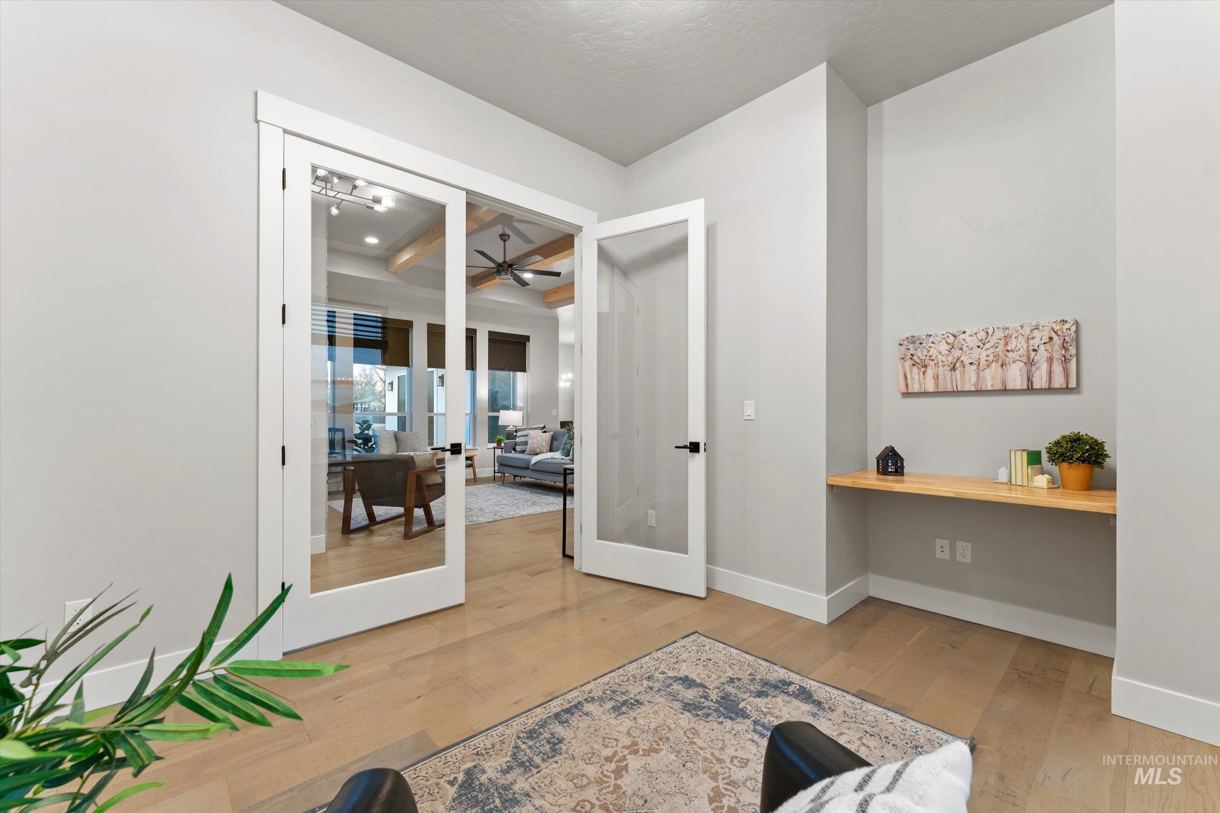 Office area with light wood-type flooring, French doors, beamed ceiling, and a ceiling fan