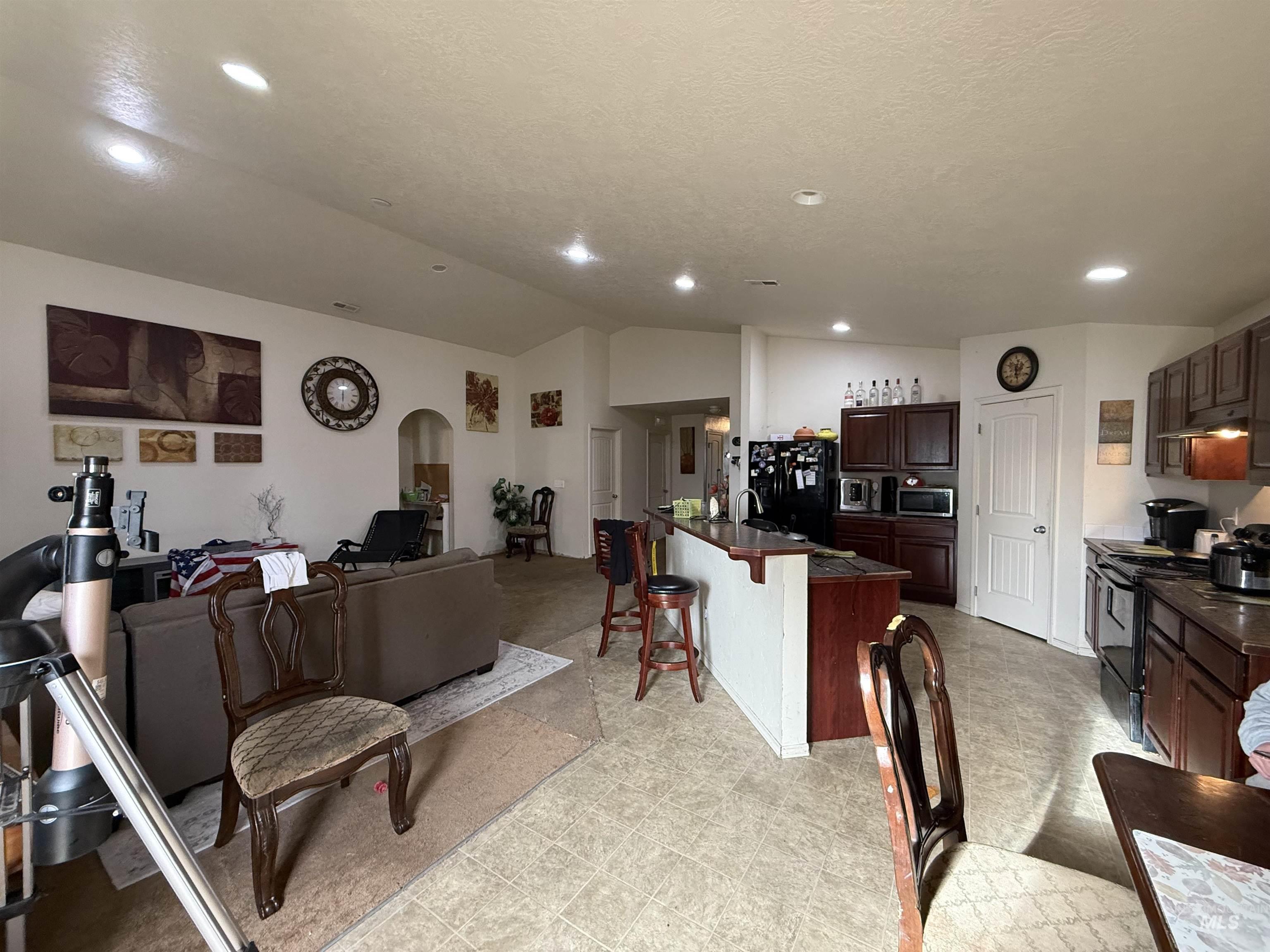 Living area with vaulted ceiling, arched walkways, light floors, recessed lighting, and a textured ceiling