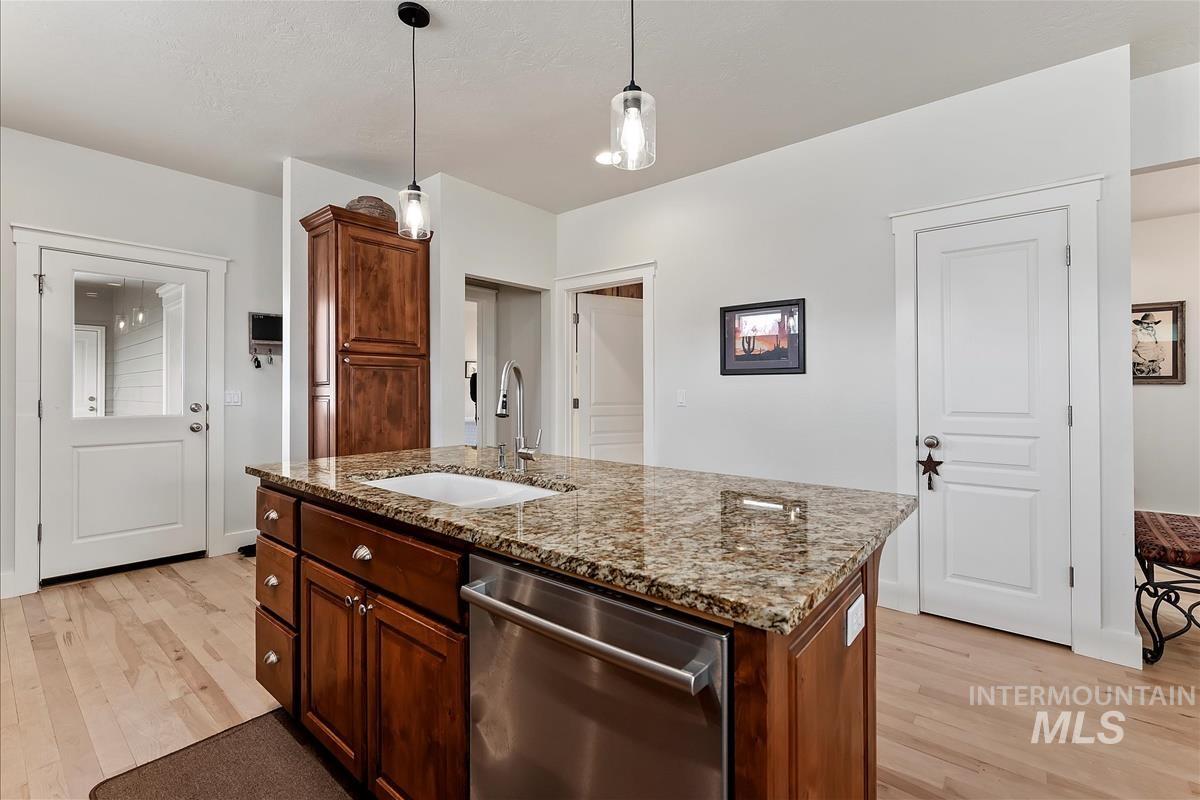 Kitchen with light stone counters, stainless steel dishwasher, an island with sink, and light wood-type flooring