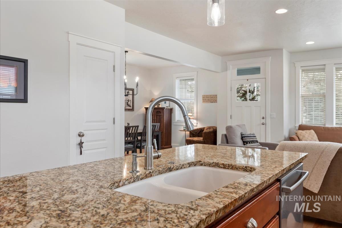 Kitchen with open floor plan, light stone counters, recessed lighting, brown cabinetry, and decorative light fixtures
