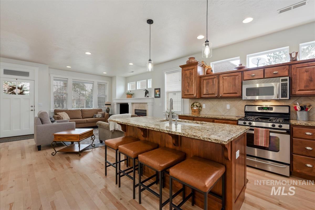 Kitchen with appliances with stainless steel finishes, hanging light fixtures, a breakfast bar, light stone counters, and a kitchen island with sink