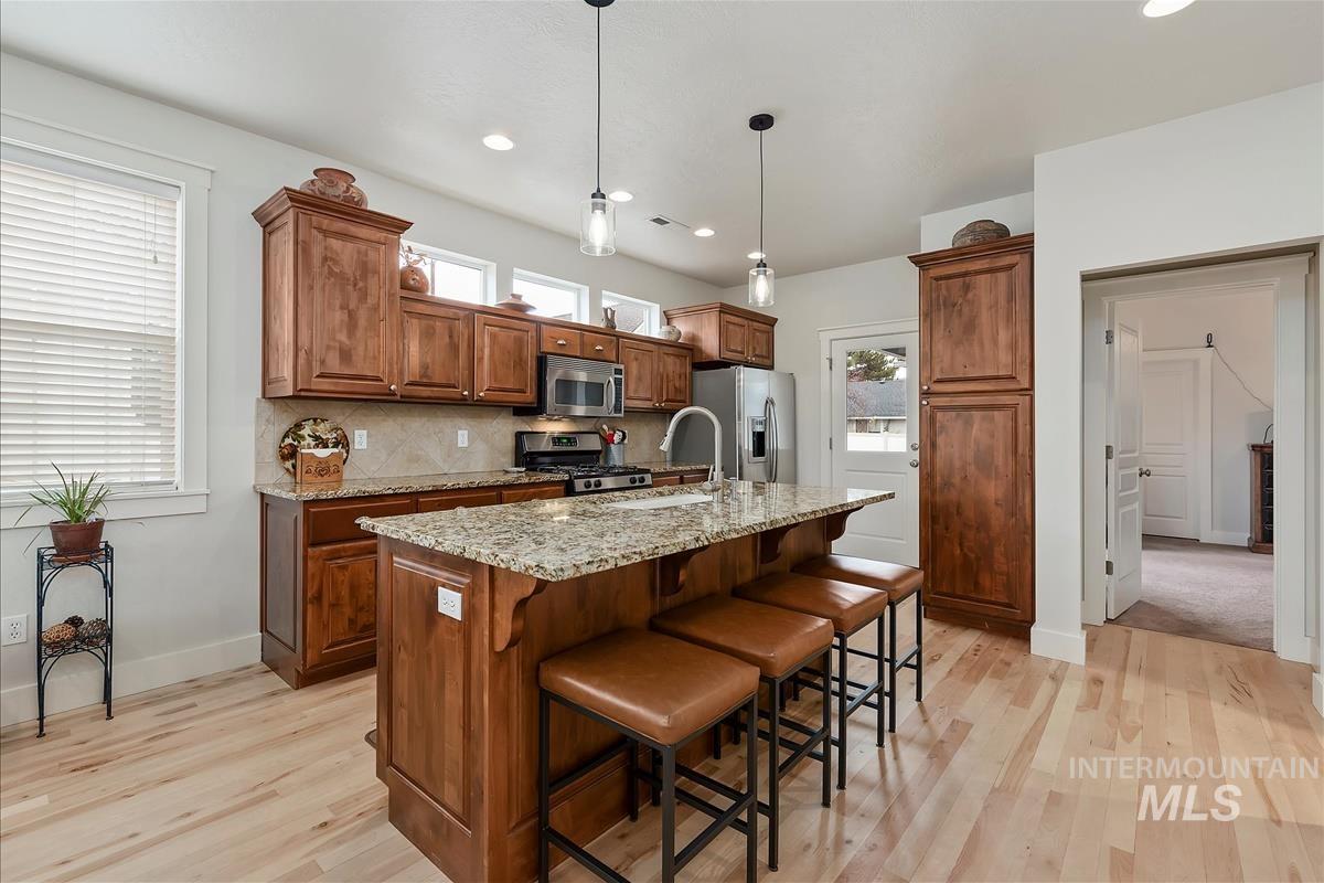 Kitchen with brown cabinets, a kitchen bar, light stone counters, hanging light fixtures, and an island with sink