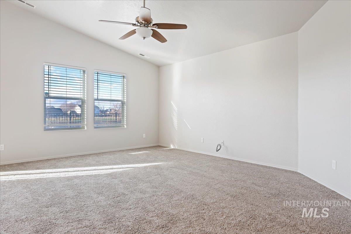 Carpeted empty room with lofted ceiling and a ceiling fan