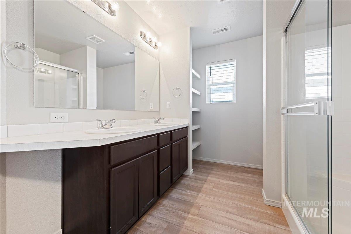 Bathroom with double vanity, a shower stall, and light wood-style flooring