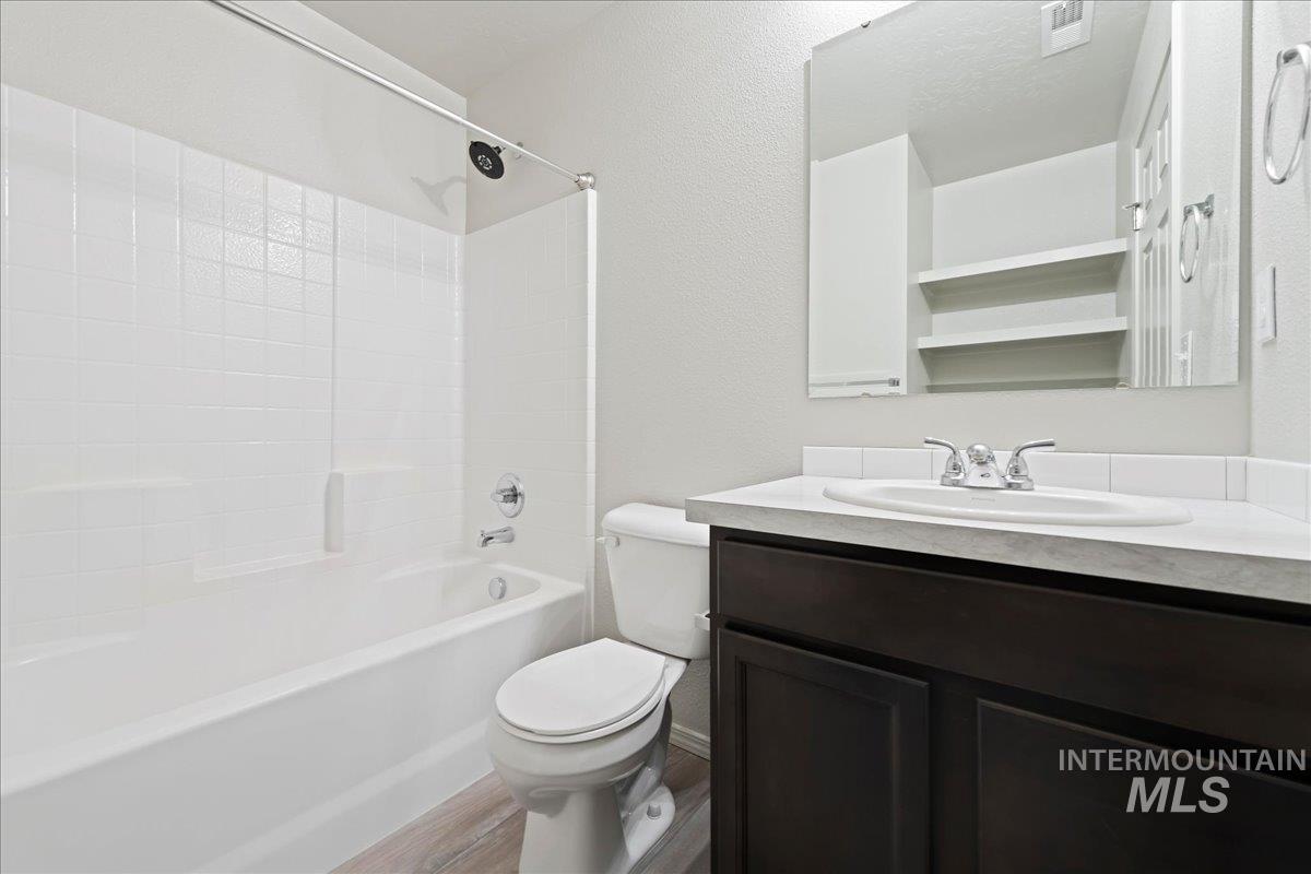 Full bathroom with vanity, shower / bath combination, light wood-style floors, and a textured wall