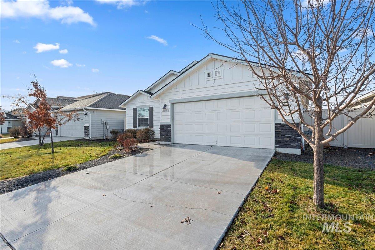 Ranch-style home featuring board and batten siding, concrete driveway, a front lawn, a garage, and stone siding