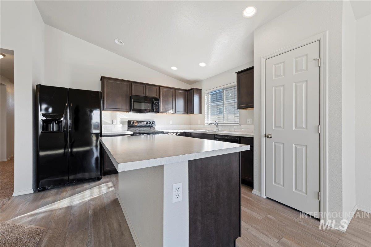 Kitchen featuring lofted ceiling, dark brown cabinetry, black appliances, light countertops, and recessed lighting