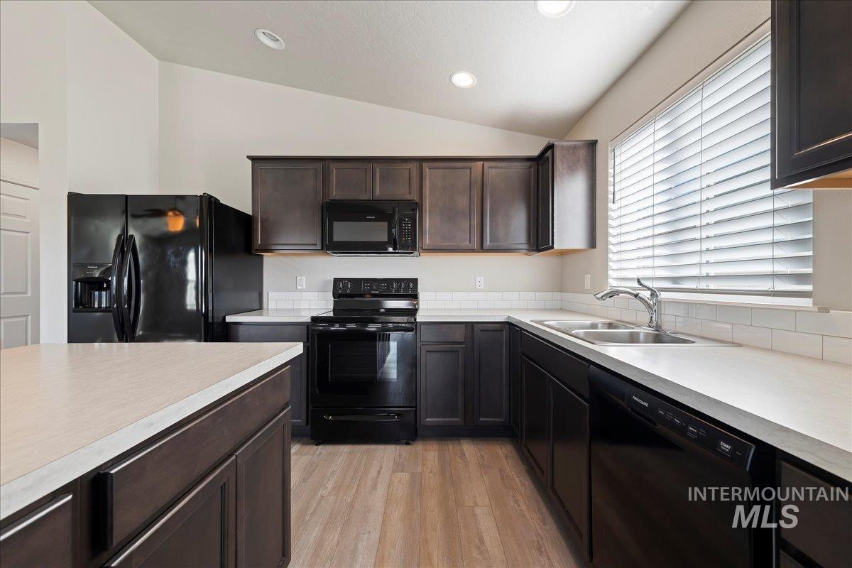 Kitchen featuring black appliances, dark brown cabinets, light countertops, vaulted ceiling, and light wood-style floors