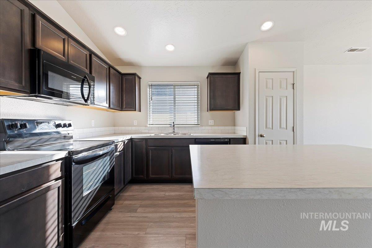 Kitchen with black appliances, dark brown cabinetry, light countertops, light wood-style floors, and recessed lighting
