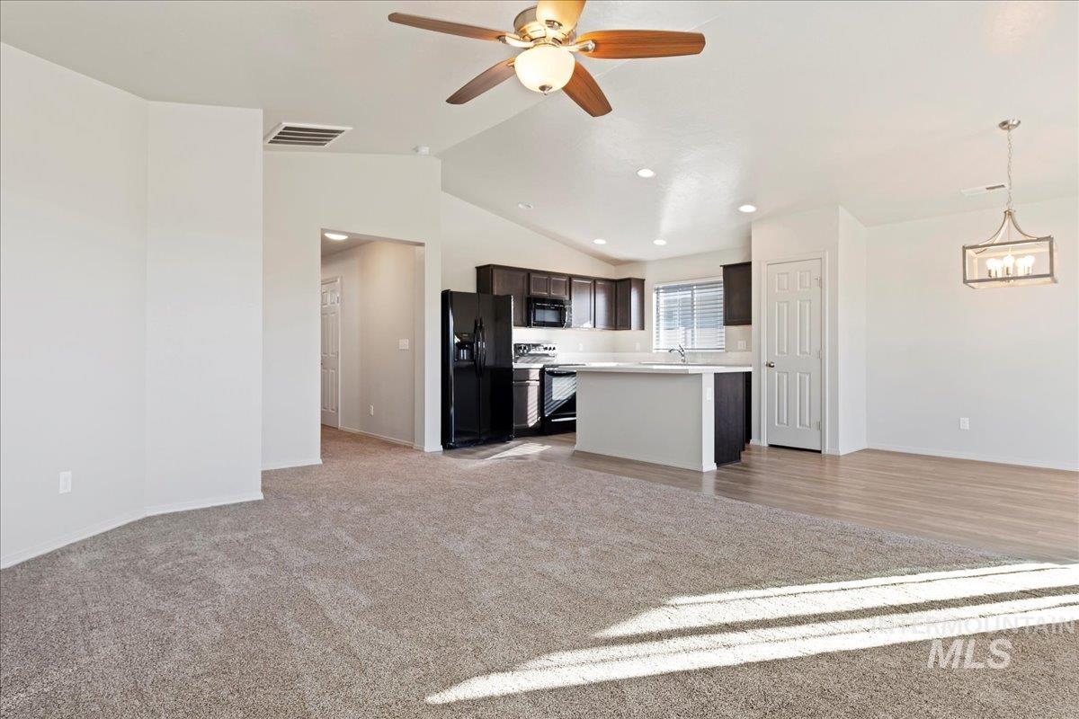 Kitchen featuring open floor plan, vaulted ceiling, black appliances, light countertops, and light colored carpet