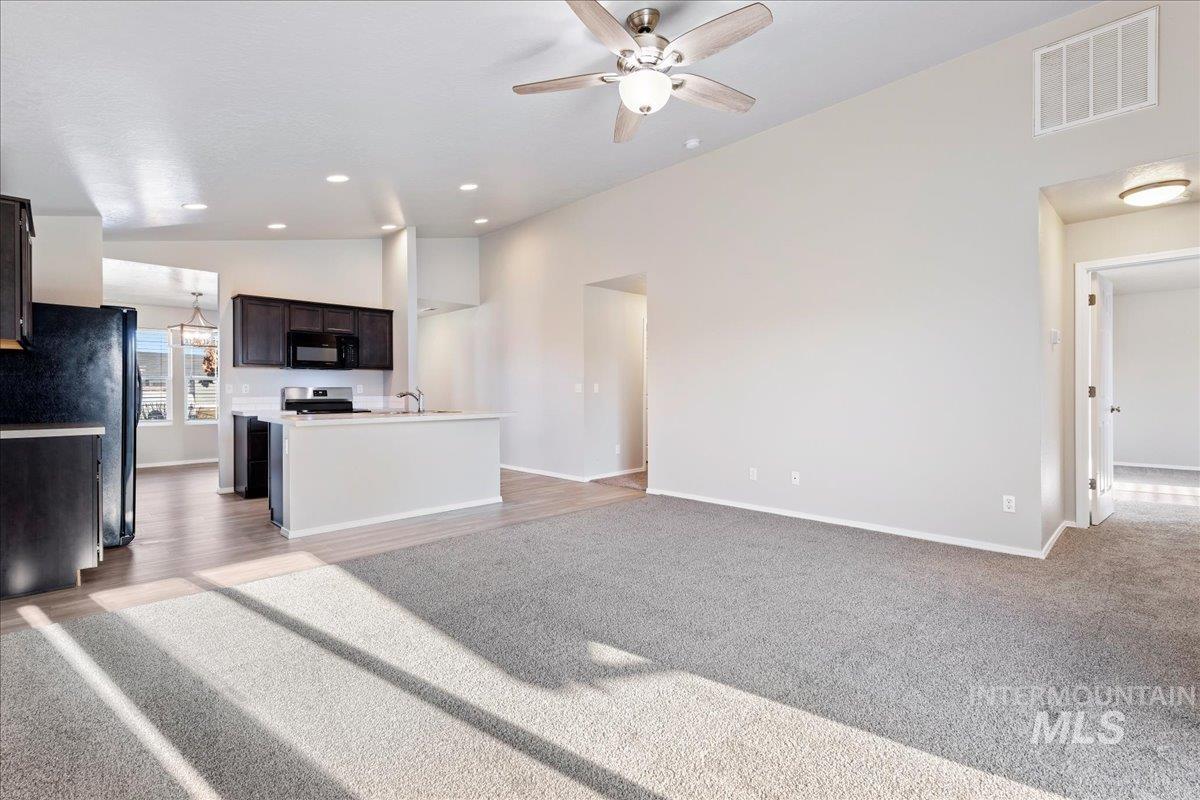 Unfurnished living room featuring a ceiling fan, light colored carpet, and high vaulted ceiling