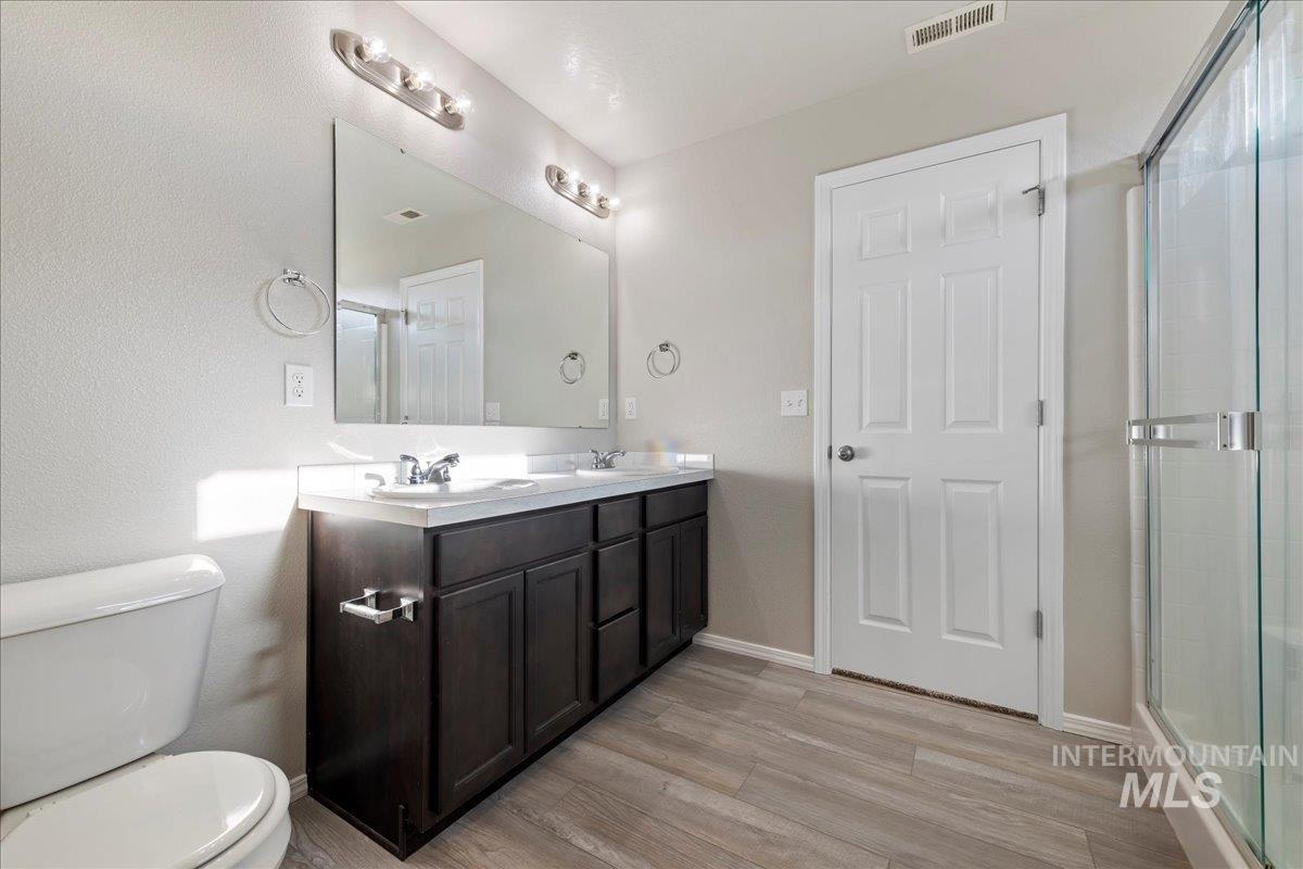 Full bath featuring double vanity, light wood-style flooring, and a shower with door