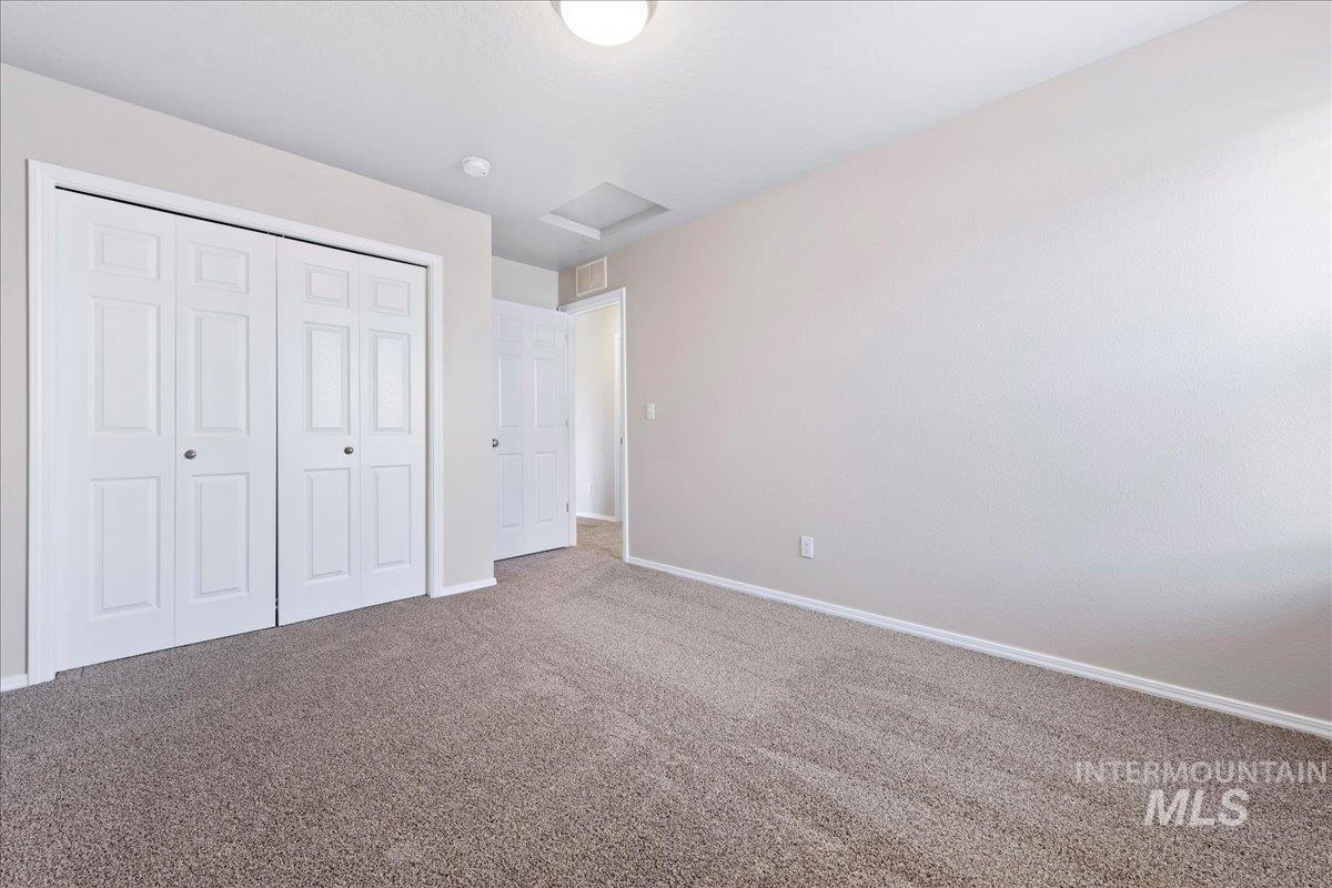 Unfurnished bedroom with attic access, carpet, and a closet