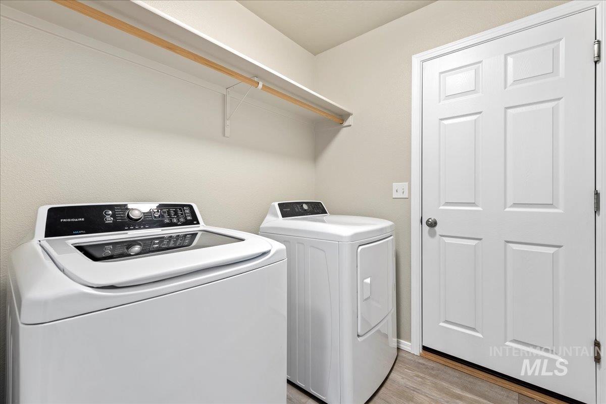 Washroom with washing machine and clothes dryer and light wood-style flooring