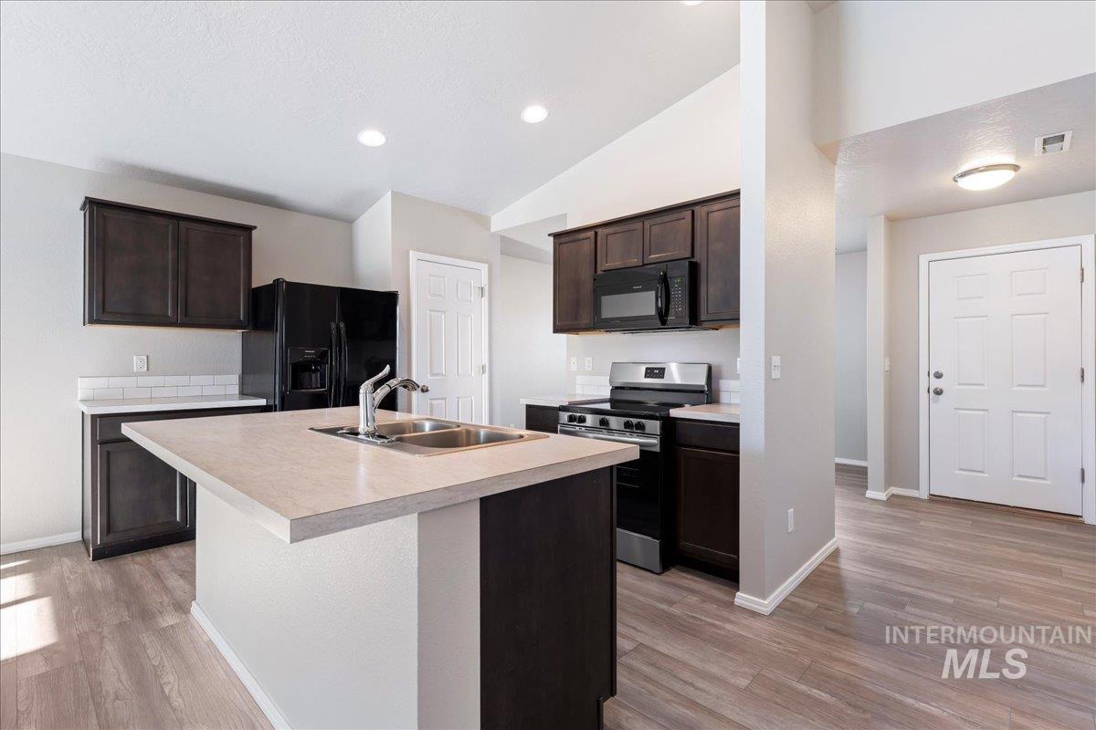 Kitchen with black appliances, dark brown cabinets, light countertops, light wood finished floors, and lofted ceiling