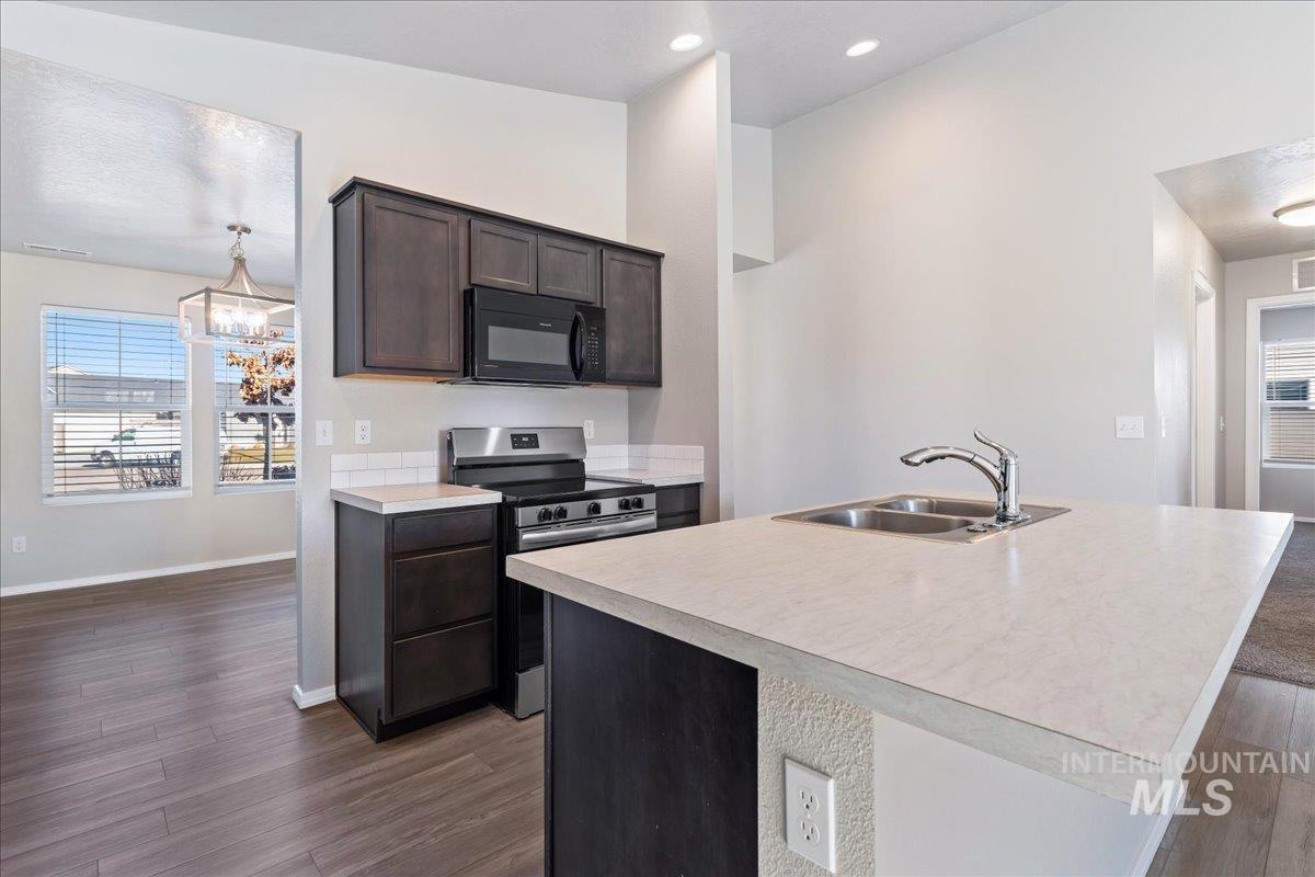 Kitchen with healthy amount of natural light, stainless steel electric range, light countertops, and an island with sink