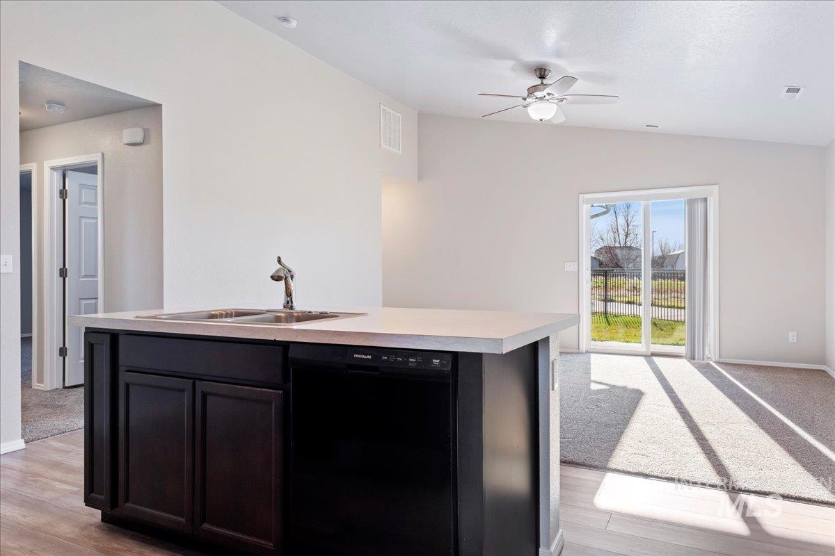 Kitchen featuring light countertops, black dishwasher, a center island with sink, vaulted ceiling, and a ceiling fan