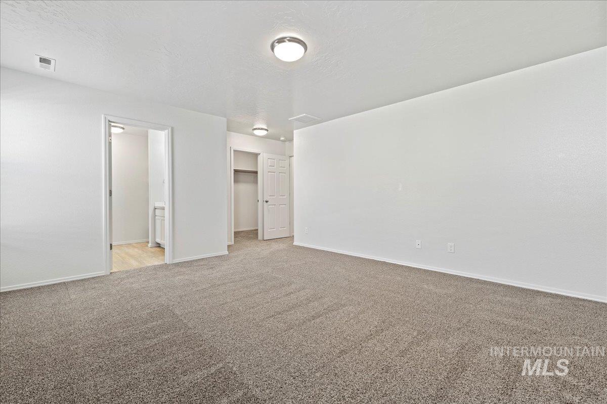 Unfurnished bedroom with a walk in closet, a textured ceiling, light carpet, and ensuite bath