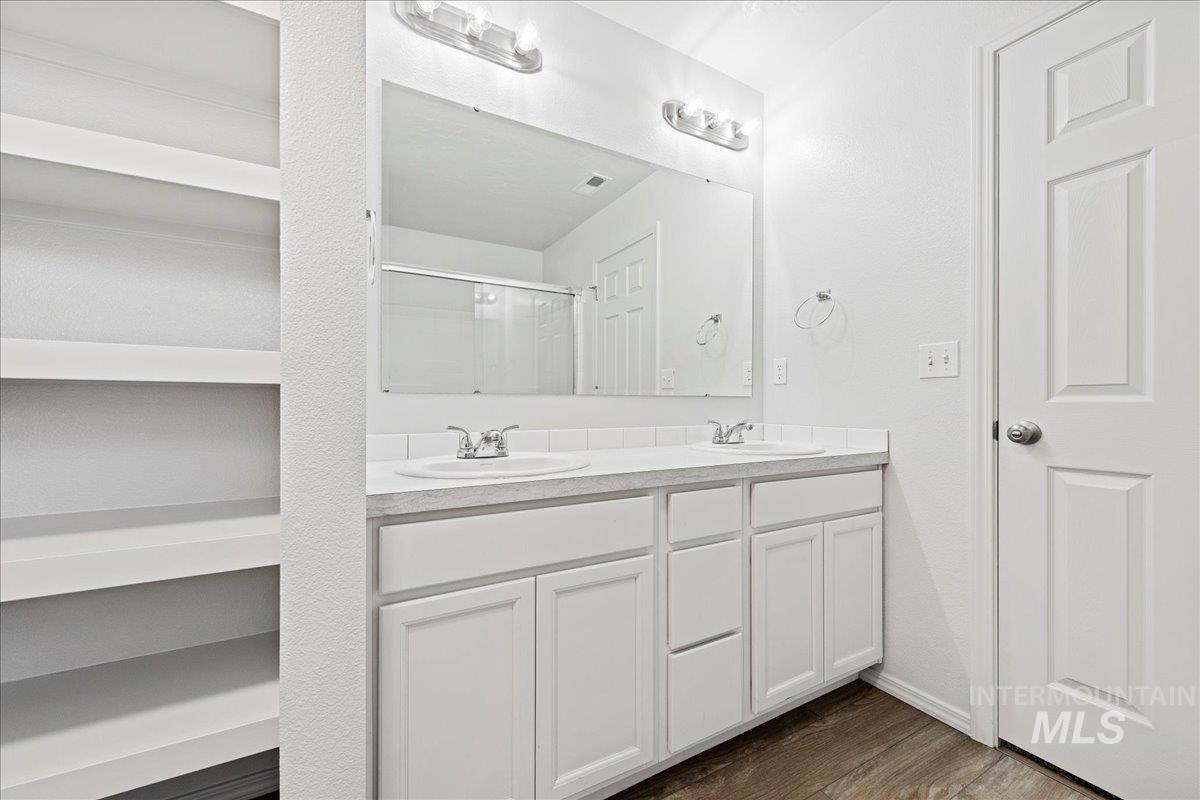 Full bathroom with double vanity, a stall shower, and dark wood finished floors