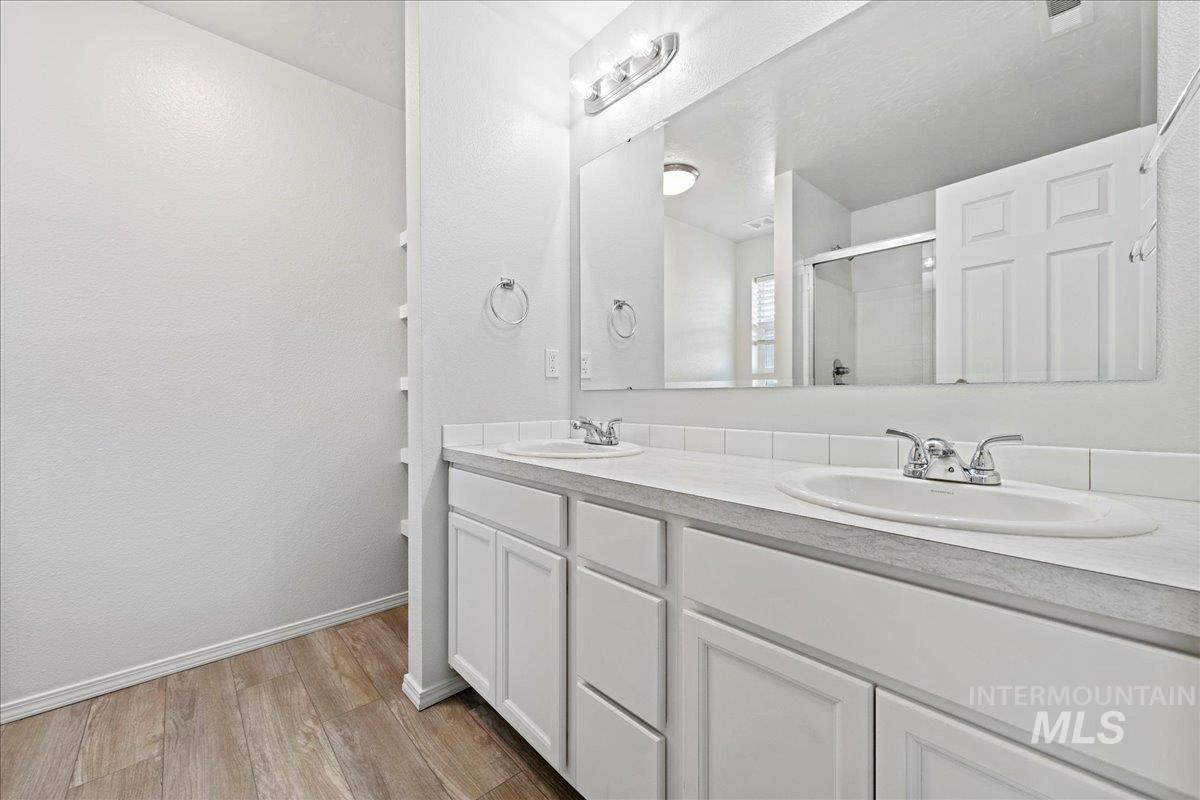 Full bathroom with double vanity, light wood-style floors, and a stall shower