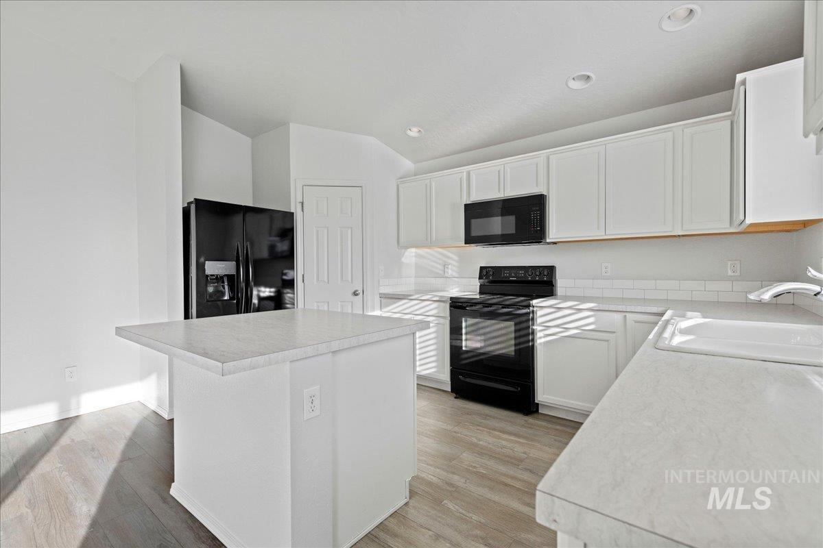 Kitchen with light countertops, black appliances, white cabinetry, a center island, and light wood-style floors