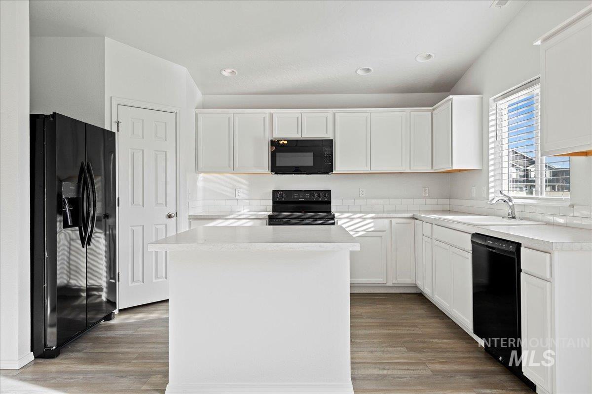 Kitchen featuring white cabinetry, black appliances, light countertops, a center island, and light wood-style floors