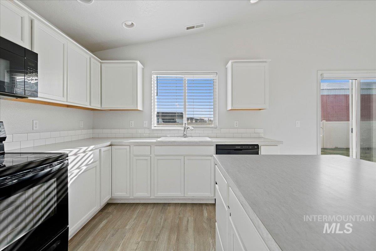 Kitchen featuring black appliances, light countertops, white cabinets, light wood finished floors, and vaulted ceiling