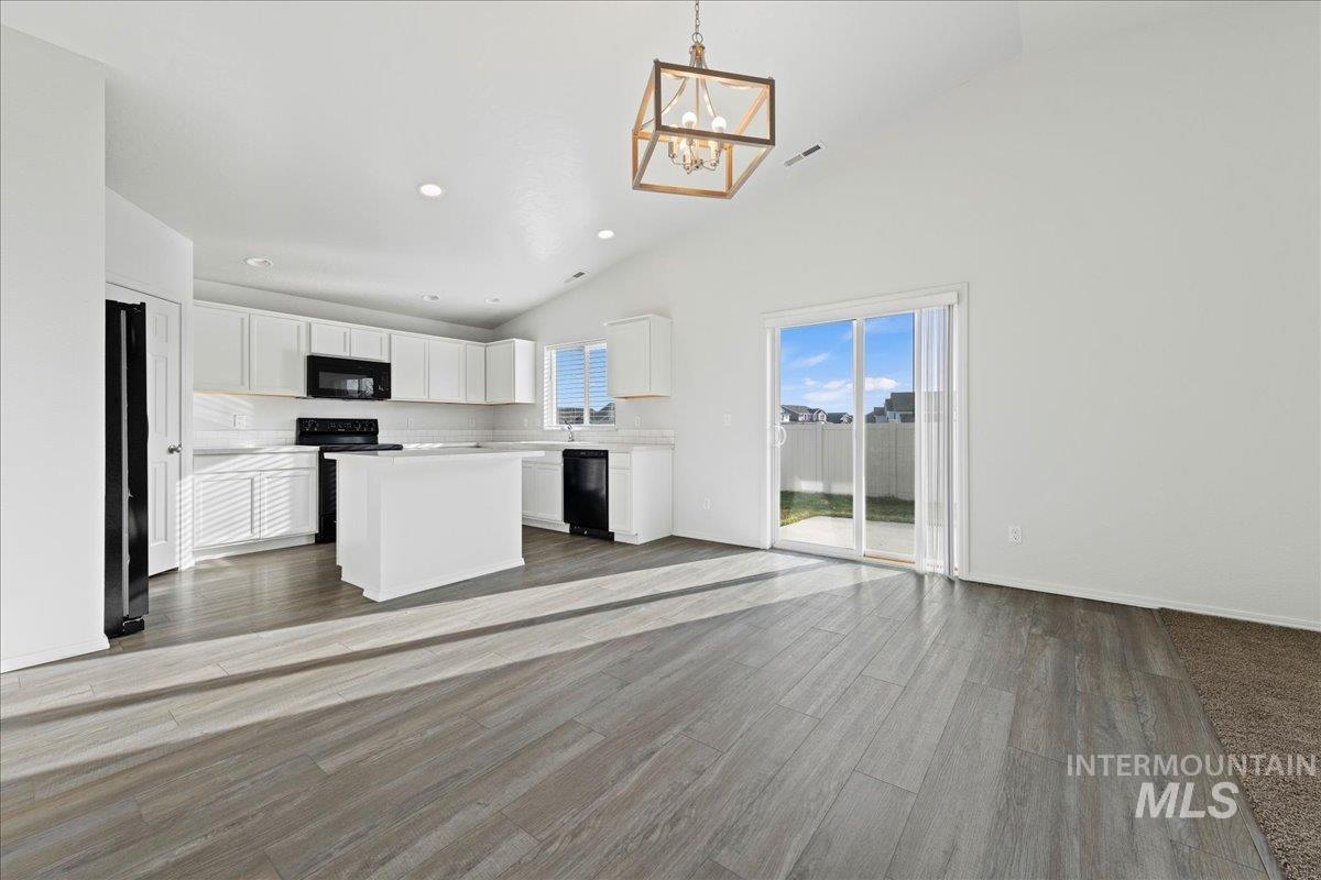 Kitchen with lofted ceiling, a kitchen island, pendant lighting, light countertops, and open floor plan