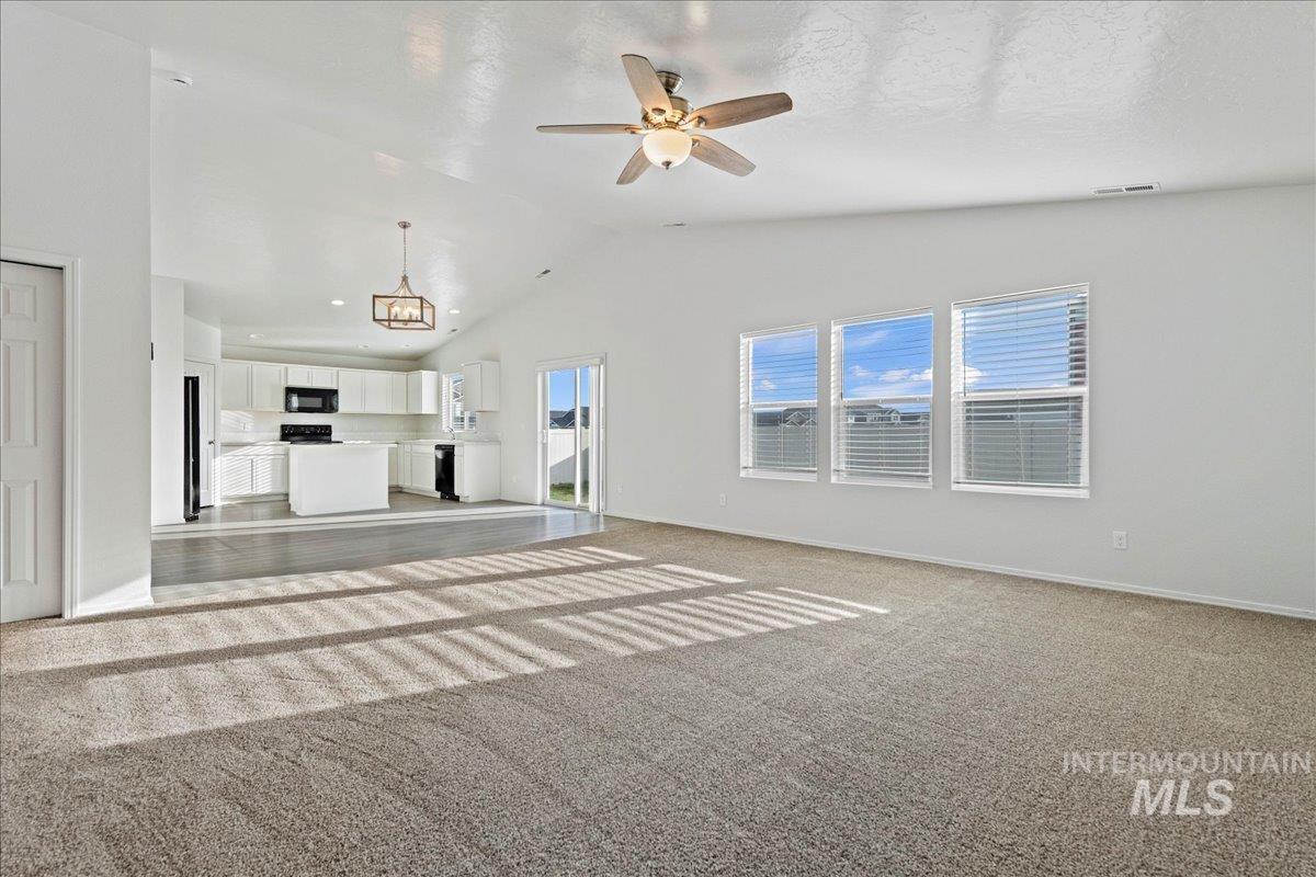 Unfurnished living room featuring ceiling fan, light colored carpet, and vaulted ceiling