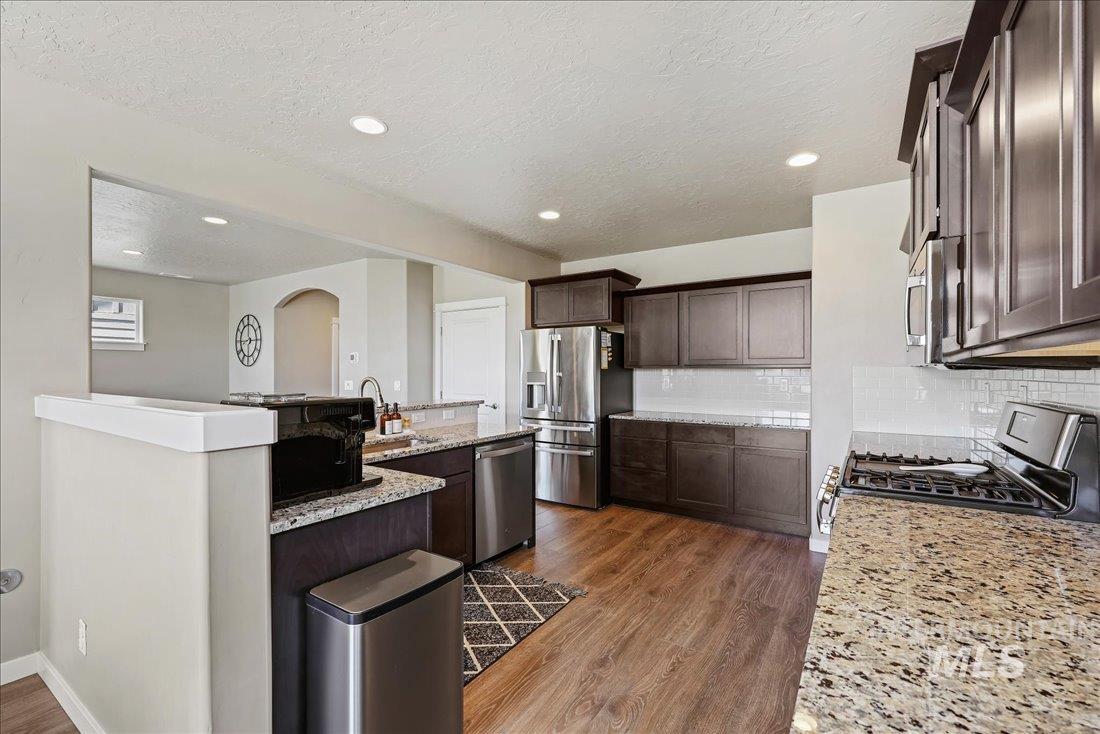 Kitchen with dark brown cabinetry, stainless steel appliances, a textured ceiling, dark wood-style floors, and light stone counters