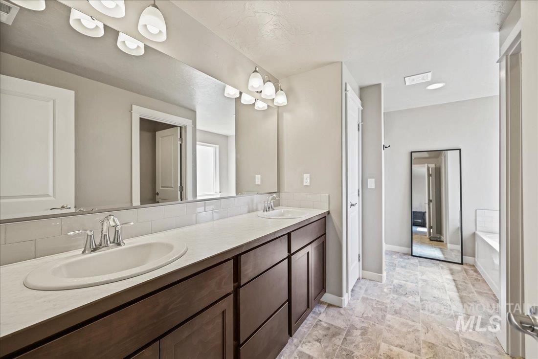 Full bathroom with double vanity, a tub to relax in, and stone finish floors