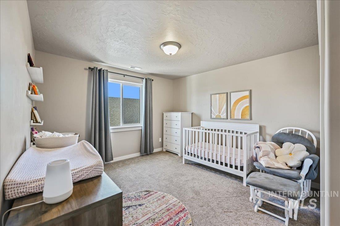 Bedroom with a textured ceiling, a nursery area, and light carpet