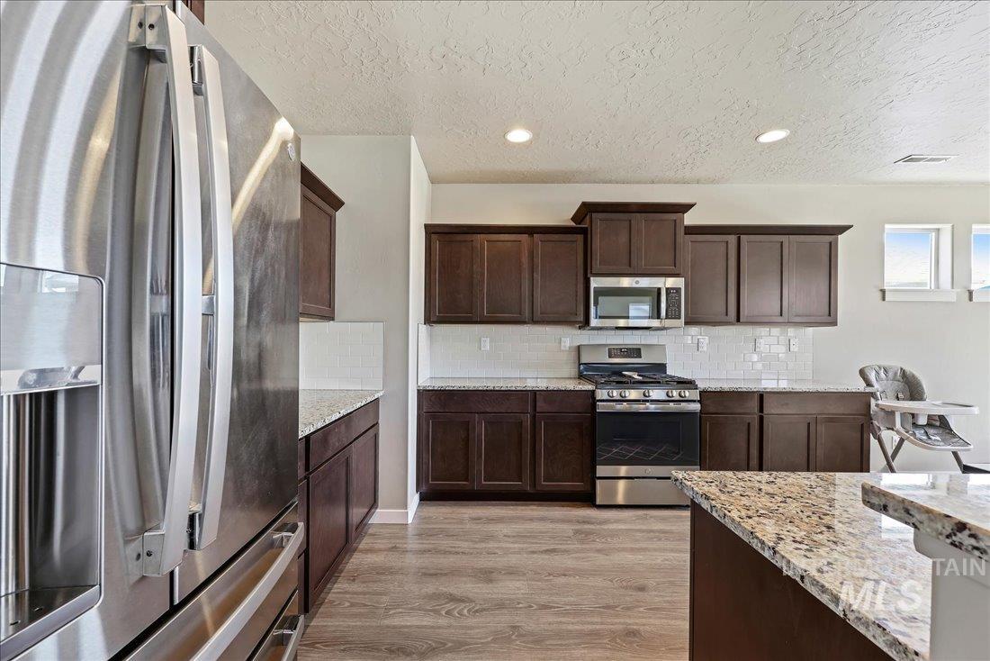 Kitchen with stainless steel appliances, light stone countertops, recessed lighting, dark brown cabinetry, and light wood-type flooring