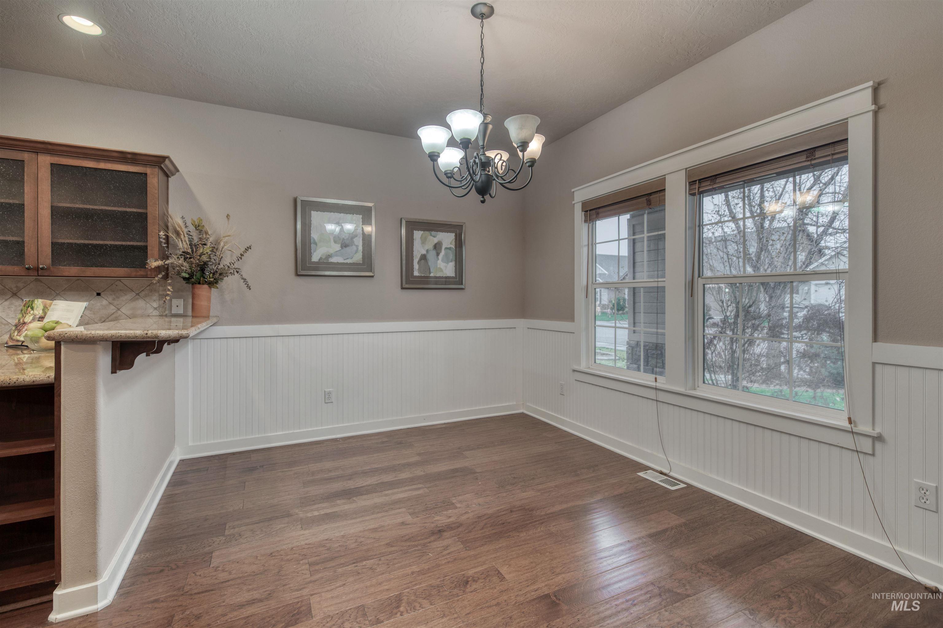 Unfurnished dining area featuring dark wood-style floors, a chandelier, and wainscoting
