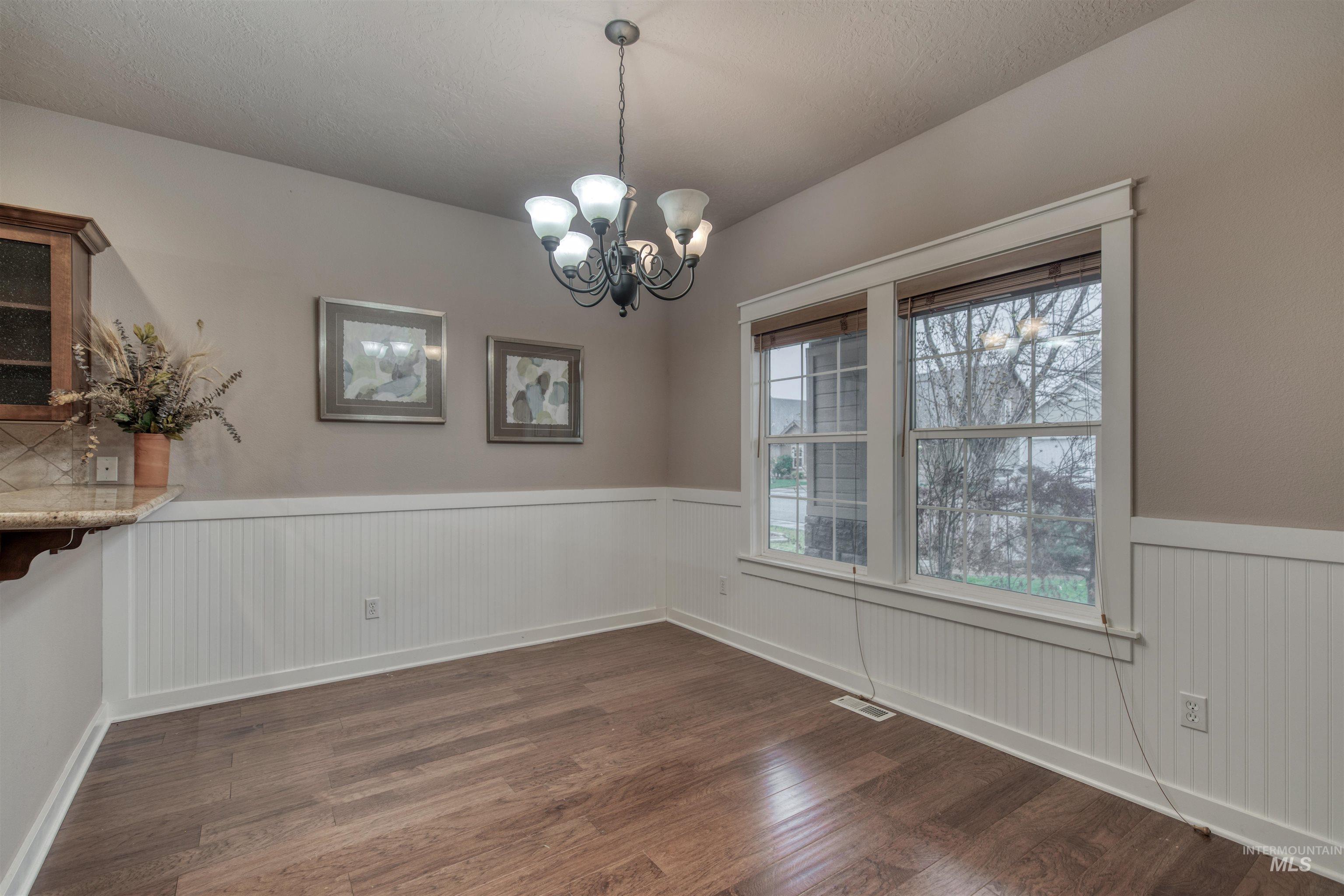 Unfurnished dining area featuring dark wood finished floors, a chandelier, and wainscoting