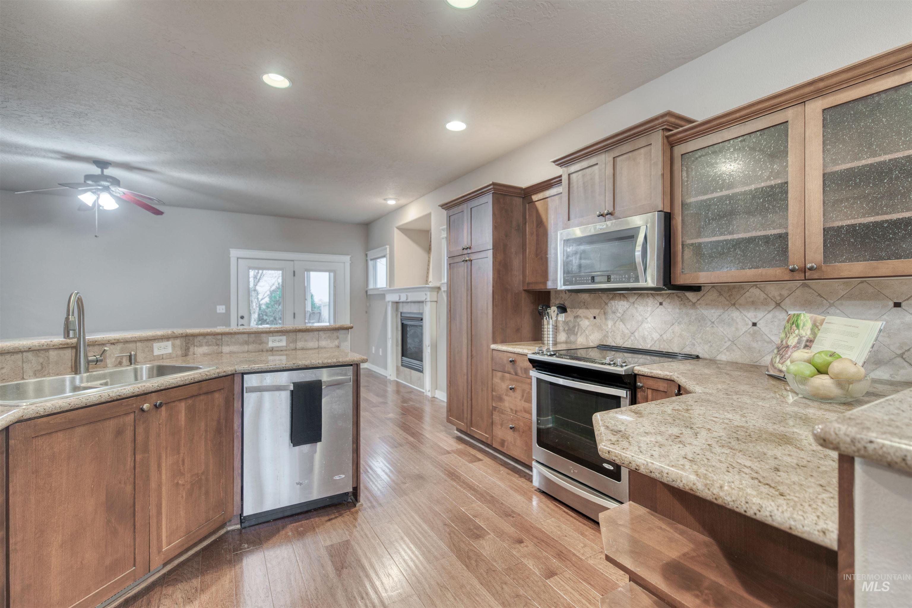 Kitchen featuring appliances with stainless steel finishes, glass insert cabinets, tasteful backsplash, brown cabinets, and recessed lighting